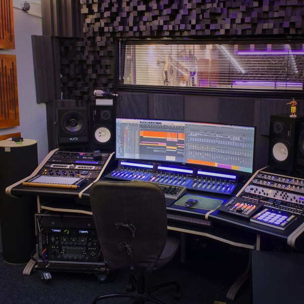 Foto von der Tonregie im StudioCarbon Tonstudio - Wiener Neudorf bei Mödling. Zu sehen sind ein Studiotisch bestückt mit Studiolautsprechern, einem sehr breiten Computerbildschirm, sowie einigen analogen 19" Studiogeräten