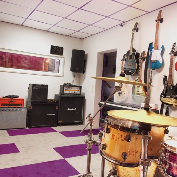 Foto von Aufnahmeraum 1 im StudioCarbon Tonstudio - Wiener Neudorf bei Mödling. Zu sehen sind ein Schlagzeug, mehrere Gitarrenverstärker sowie einige Gitarren an Wandhalterungen. Sicht auf das Regiefenster