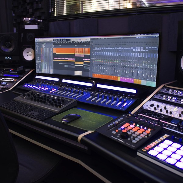Foto von der Tonregie im StudioCarbon Tonstudio - Wiener Neudorf bei Mödling. Zu sehen sind ein Studiotisch bestückt mit Studiolautsprechern, einem sehr breiten Computerbildschirm, sowie einigen analogen 19" Studiogeräten